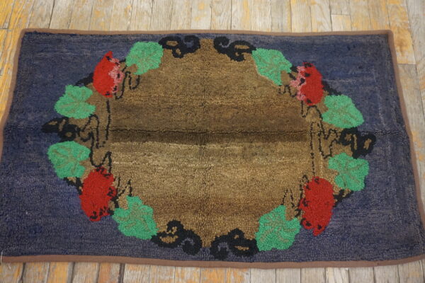 Looped pile rug in blue, brown, red, and green with a decorative fruit and leaf border on wood planks.