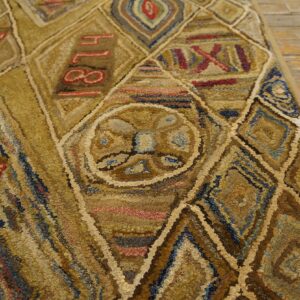 Highly textured gold and brown rug with red numbers and geometric shapes on distressed wood floor.