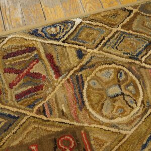 Textured beige and brown hooked rug with abstract geometric patterns rests on worn wooden floorboards.