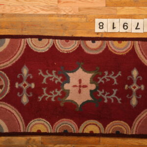 Deep red rug with stylized floral motifs and multicolored scalloped borders lies on hardwood flooring.