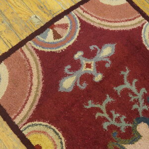 Distressed red shag rug featuring muted gray, yellow, and pink motifs rests on worn wood floorboards.