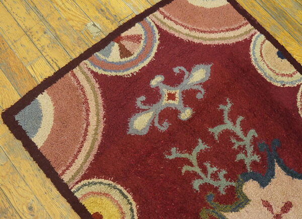 Distressed red shag rug featuring muted gray, yellow, and pink motifs rests on worn wood floorboards.
