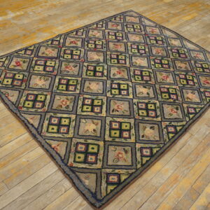 A grayish-blue hooked rug featuring a grid of flowers and geometric boxes rests on distressed yellow wood planks.