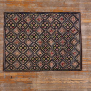 Taupe rug displaying a multicolored floral and geometric diamond grid pattern rests on rustic wood planks.