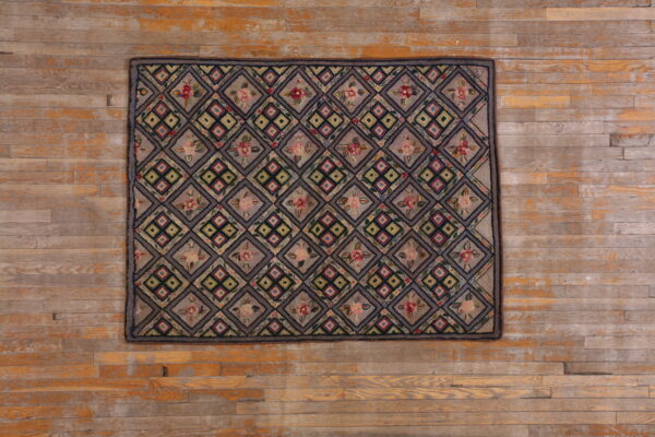 Taupe rug displaying a multicolored floral and geometric diamond grid pattern rests on rustic wood planks.