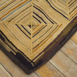 Textured rug corner featuring diagonal stripes in gold, cream, navy, and burgundy on distressed wood.