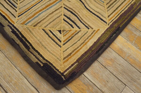 Textured rug corner featuring diagonal stripes in gold, cream, navy, and burgundy on distressed wood.