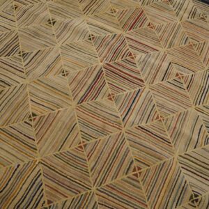Muted multi-colored striped rug with a repeating geometric diamond pattern on light wood floors.