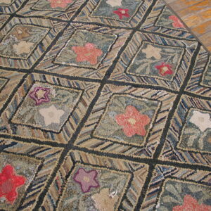 Highly textured rug with floral diamonds in red, pink, and beige on a green and blue background, resting on wood flooring.