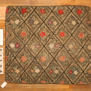 Earth-toned hooked rug with a dark diamond grid containing multicolored floral patterns on wood planks.