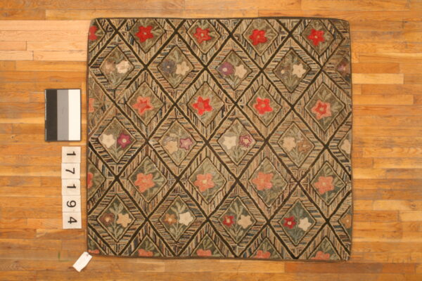 Earth-toned hooked rug with a dark diamond grid containing multicolored floral patterns on wood planks.