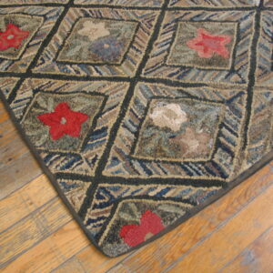Coarse-textured rug featuring a dark diamond grid, multicolored stripes, and red floral motifs on wood flooring.