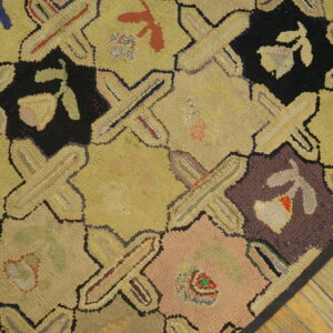 Yellow, black, and multicolored hooked rug with a geometric lattice design sits on light wood flooring.