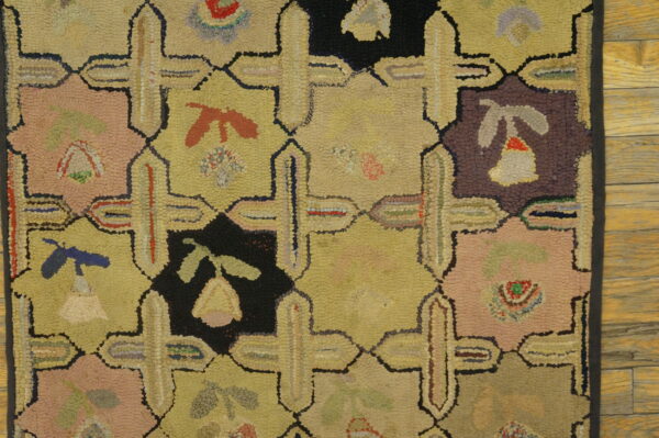 Tan, pink, black, and blue looped rug featuring a geometric grid pattern on rustic hardwood planks.