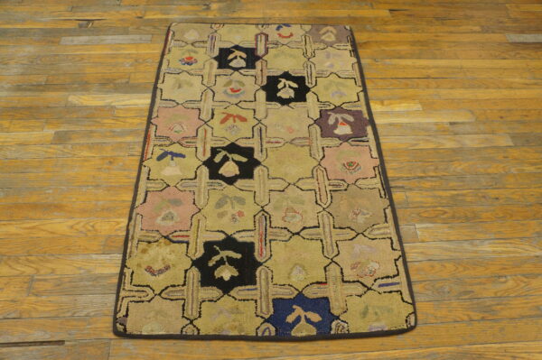 Tan, pink, black, and blue looped rug featuring a geometric grid pattern on rustic hardwood planks.
