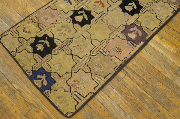 Low-pile hooked rug with multicolored geometric patches and crosses resting on rustic wood plank flooring.