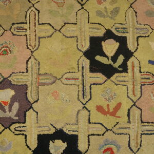 Multicolor hooked rug detail with repeating geometric panels in yellow, pink, black, and maroon over wood floor.