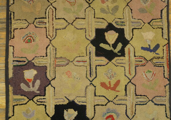 Multicolor hooked rug detail with repeating geometric panels in yellow, pink, black, and maroon over wood floor.