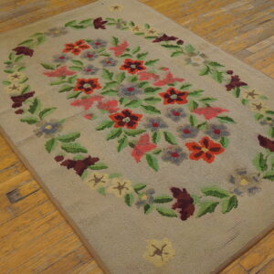 Low pile beige rug with a red, pink, and green floral wreath pattern sits on a worn hardwood floor.
