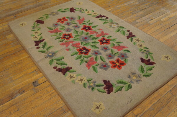 Low pile beige rug with a red, pink, and green floral wreath pattern sits on a worn hardwood floor.