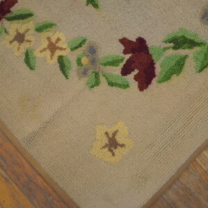 Textured beige rug featuring colorful hooked flowers and leaves on distressed wood flooring.