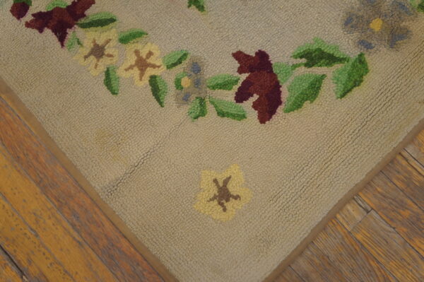 Textured beige rug featuring colorful hooked flowers and leaves on distressed wood flooring.
