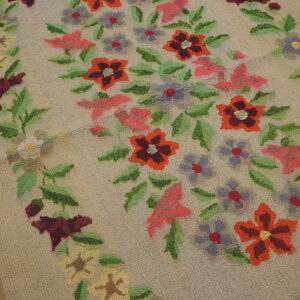 Low-pile beige hooked rug featuring a colorful vertical floral garland on distressed wooden flooring.