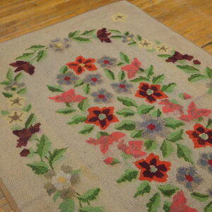 Low-pile beige rug with a colorful floral garland design rests on distressed wooden floorboards.