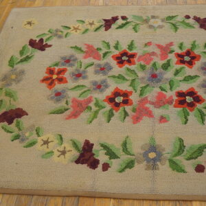 Loop-pile tan rug with a colorful floral medallion in red, pink, and green, resting on worn plank wood.