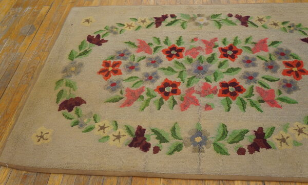 Loop-pile tan rug with a colorful floral medallion in red, pink, and green, resting on worn plank wood.