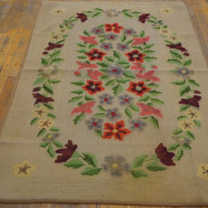 Beige looped rug with a colorful floral medallion in red, pink, and green, set on distressed wood flooring.