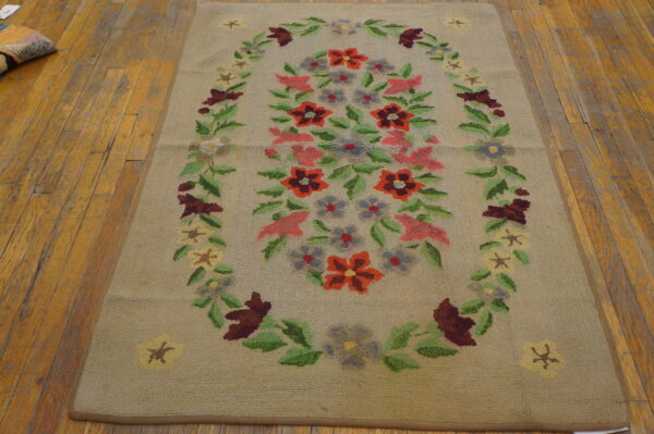 Beige looped rug with a colorful floral medallion in red, pink, and green, set on distressed wood flooring.