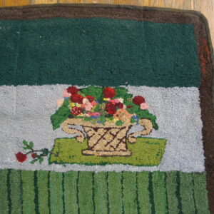 Hooked rug with multicolored floral basket design over striped green and gray sections on wood planks.
