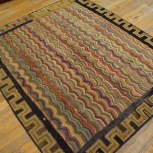 A multicolored rug with wavy stripes and a black and gold geometric key border rests on wood flooring.