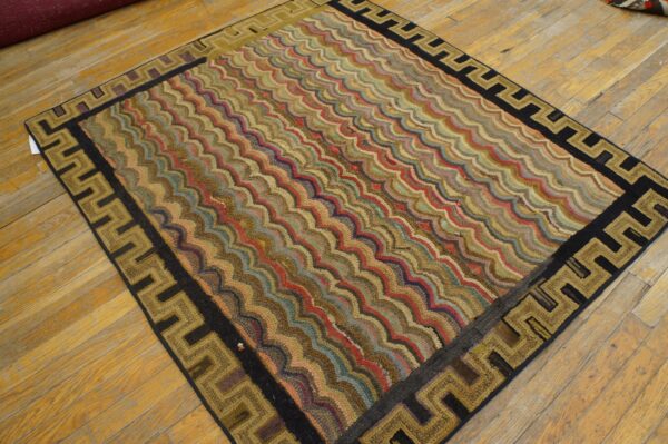 A multicolored rug with wavy stripes and a black and gold geometric key border rests on wood flooring.