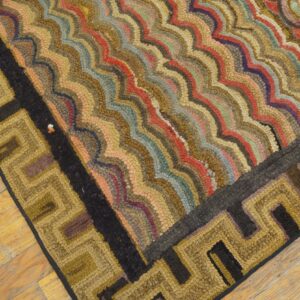 Close-up of a hooked rug featuring multicolored wavy stripes and a gold and black geometric Greek key border on wood flooring.