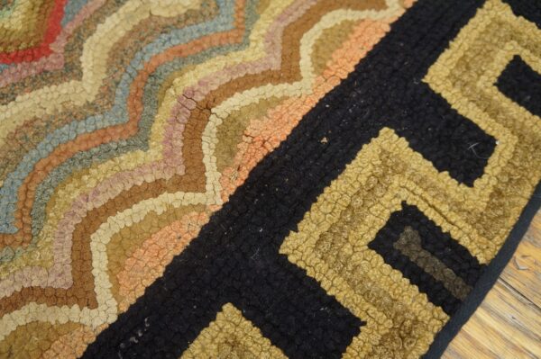 Textured rug with multicolored curved bands transitioning into a chunky black and gold geometric pattern.