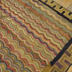 Multicolored high-pile rug with a wavy design and geometric border rests on rustic wood flooring.