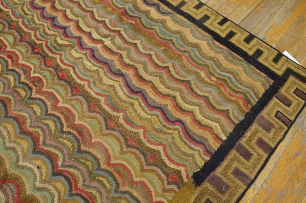 Multicolored high-pile rug with a wavy design and geometric border rests on rustic wood flooring.