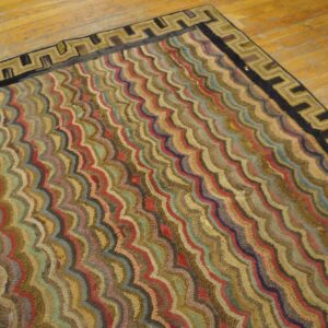 A textured rug with multicolored wavy stripes and a black and tan Greek key border lies on a light wooden floor.