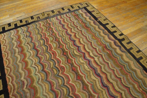 A textured rug with multicolored wavy stripes and a black and tan greek key border lies on a light wooden floor.