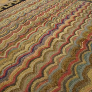 Textured rug with colorful wavy stripes and a prominent geometric key border on wood flooring.