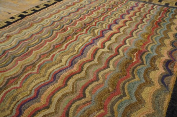 Textured rug with colorful wavy stripes and a prominent geometric key border on wood flooring.