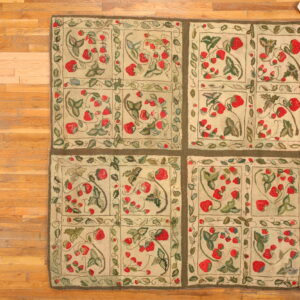 Textured beige rug with a repeating motif of red strawberries and green leaves on natural wood plank flooring.