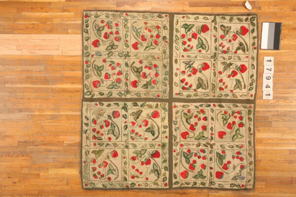 Textured beige rug with a repeating motif of red strawberries and green leaves on natural wood plank flooring.