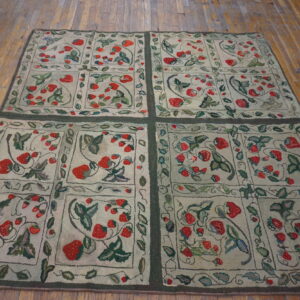 Low-pile rug with red strawberry and green leaf patterns is divided into squares over distressed wood flooring.