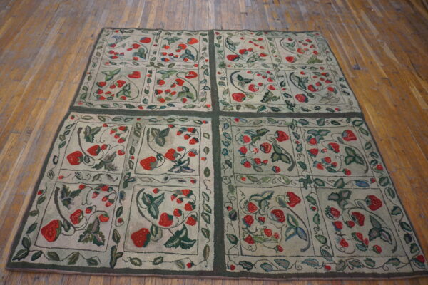 Low-pile rug with red strawberry and green leaf patterns is divided into squares over distressed wood flooring.