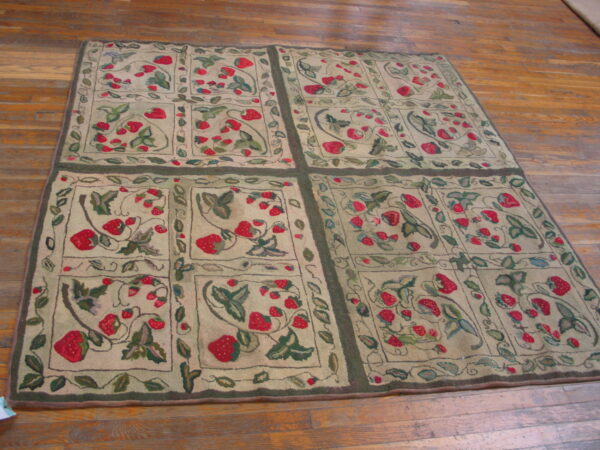 Beige rug featuring a detailed red strawberry and green leaf pattern framed by dark borders on wood floor.