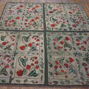 Low pile rug with a red strawberry botanical pattern and green grid borders on brown wood floors.