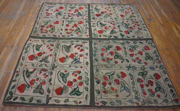 Low pile rug with a red strawberry botanical pattern and green grid borders on brown wood floors.